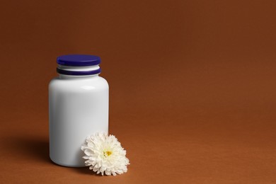 Photo of Medicine bottle and beautiful flower on brown background, space for text