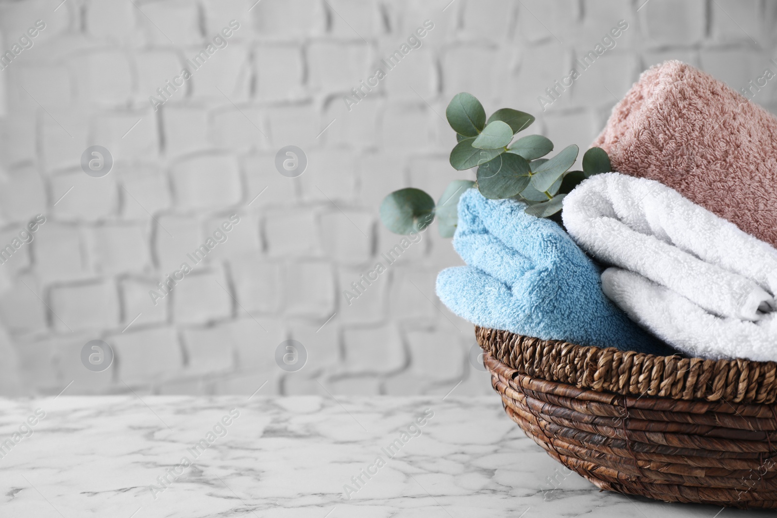 Photo of Wicker basket with folded bath towels and eucalyptus branch on white marble table. Space for text