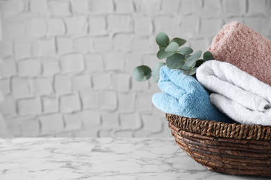 Photo of Wicker basket with folded bath towels and eucalyptus branch on white marble table. Space for text