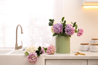 Photo of Bouquet with beautiful hydrangea flowers in can and scissors on light countertop