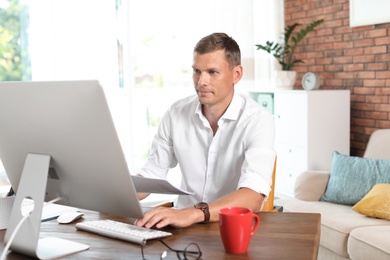 Photo of Young man working with computer in home office