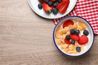 Photo of Delicious crispy cornflakes with milk and fresh berries on wooden table, flat lay. Space for text
