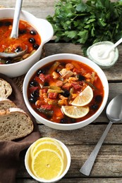 Meat solyanka soup with sausages, olives and vegetables served on wooden table, above view