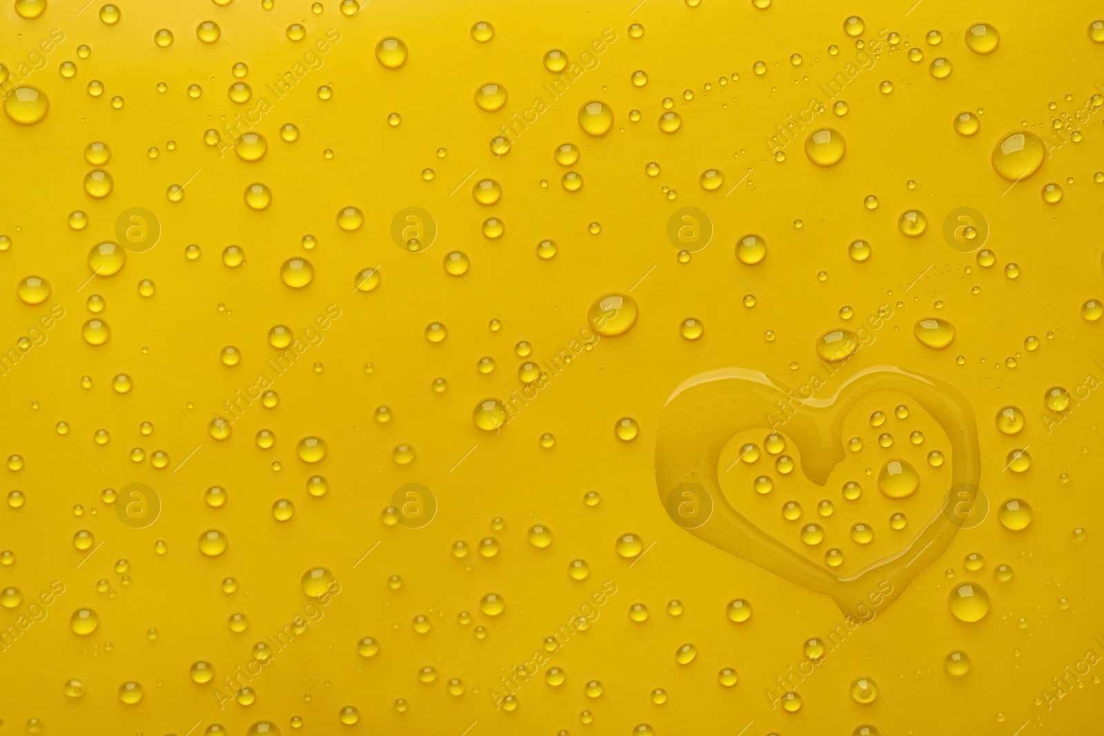 Photo of Heart shape of water and drops on yellow background, top view