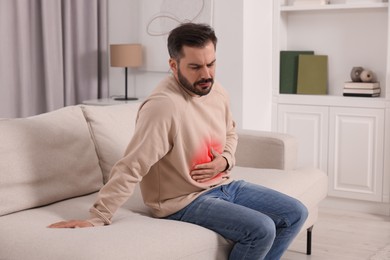 Image of Man suffering from abdominal pain on sofa at home