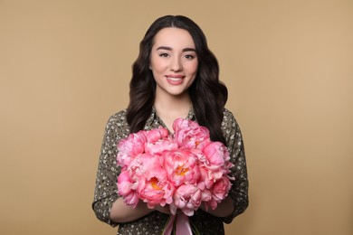 Photo of Beautiful young woman with bouquet of pink peonies on light brown background