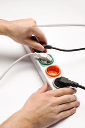 Photo of Man inserting power plug into extension cord on white background, closeup. Electrician's professional equipment