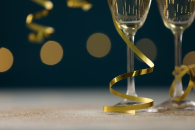 Photo of Glasses of champagne and serpentine streamers on table against blurred lights, closeup