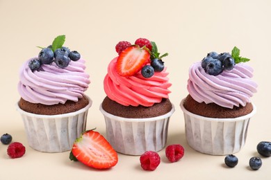 Photo of Different delicious cupcakes with cream and berries on beige background