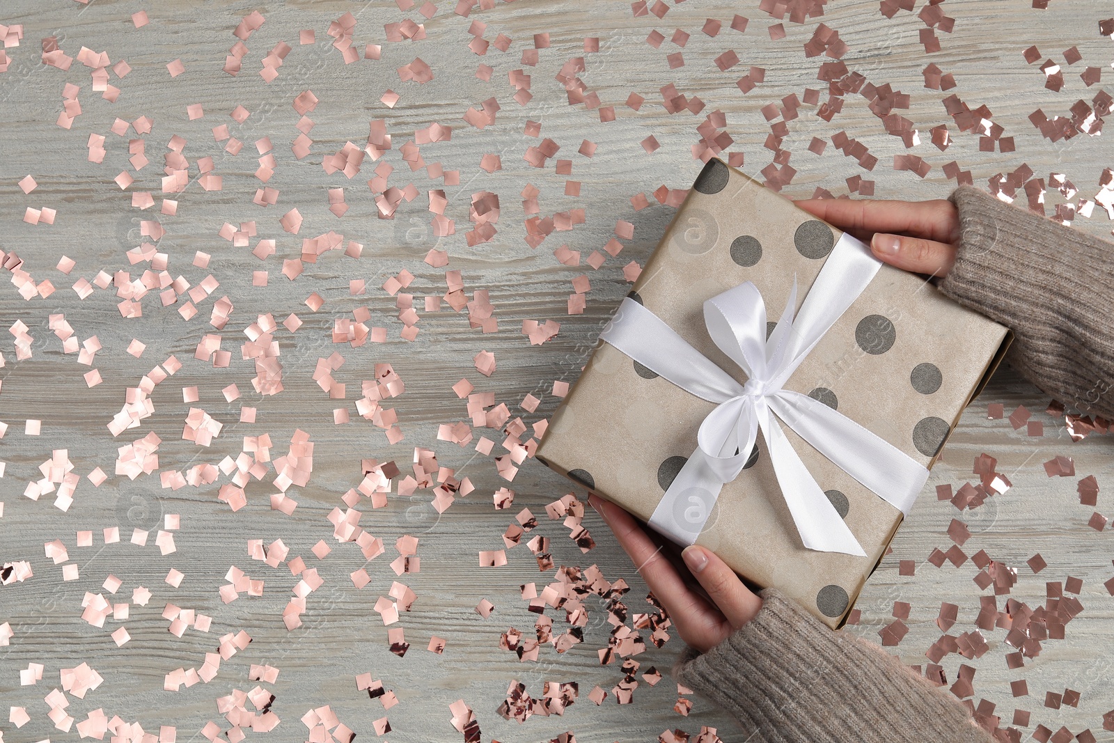 Photo of Christmas present. Woman with gift box and confetti at wooden table, top view. Space for text