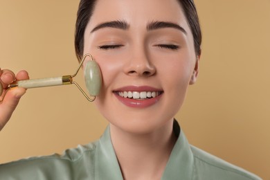 Young woman massaging her face with jade roller on beige background