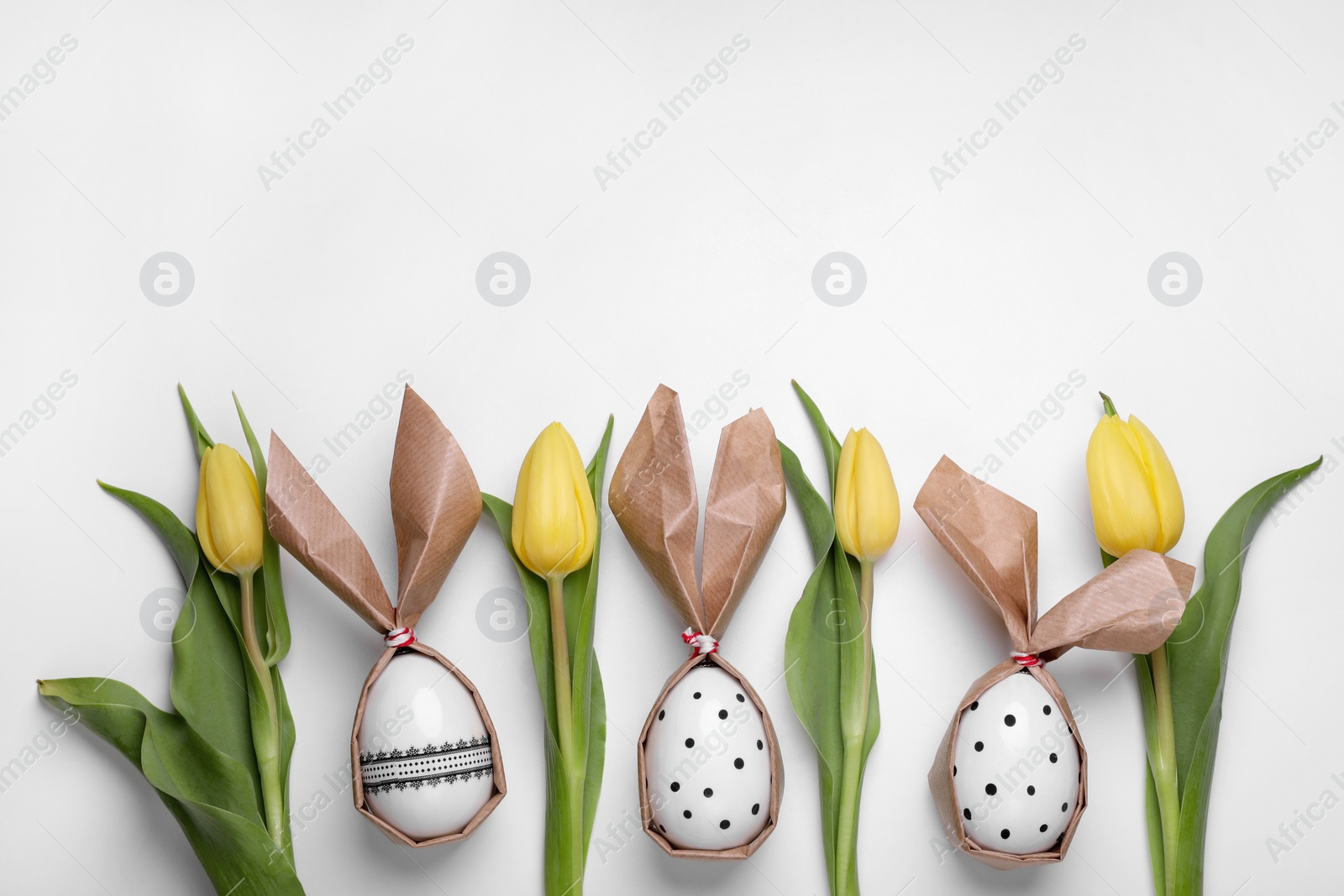 Photo of Flat lay composition with Easter bunnies made of paper and eggs on white background. Space for text