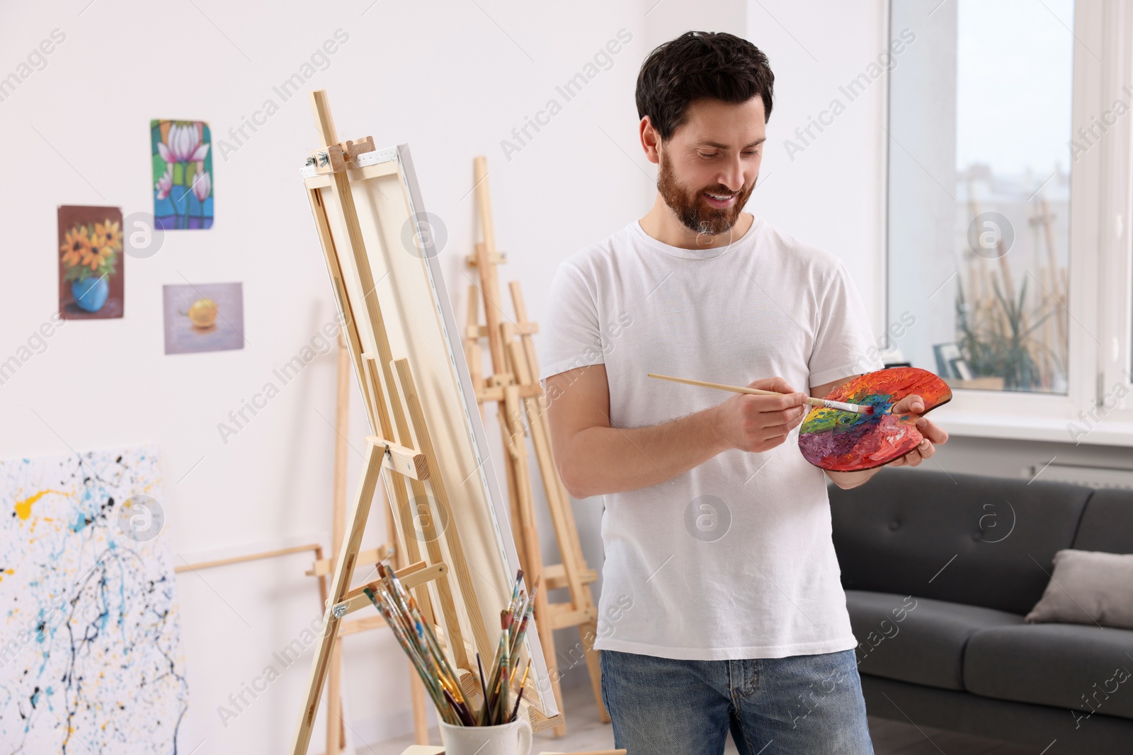 Photo of Man painting in studio. Using easel to hold canvas