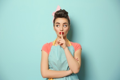 Photo of Portrait of funny young housewife showing silence gesture on color background