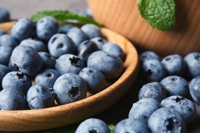 Dishware with juicy blueberries and green leaves on table, closeup