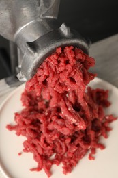Photo of Mincing beef with metal meat grinder on light table, closeup
