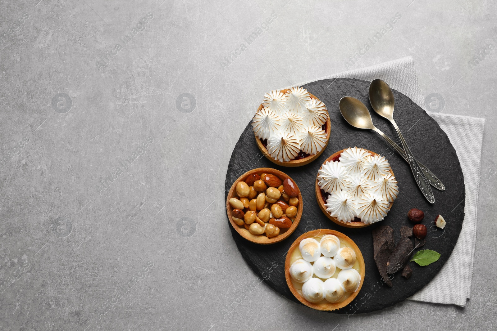 Photo of Many different tartlets served on grey table, top view and space for text. Delicious dessert