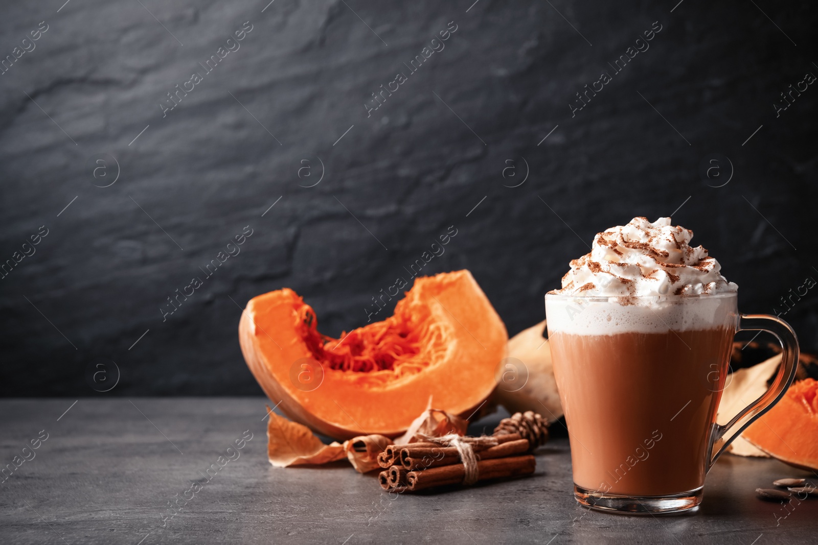 Photo of Delicious pumpkin latte and ingredients on grey table. Space for text