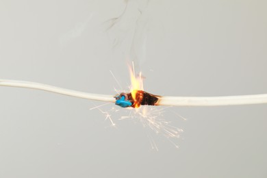 Photo of Inflamed white wire on grey background, closeup. Electrical short circuit