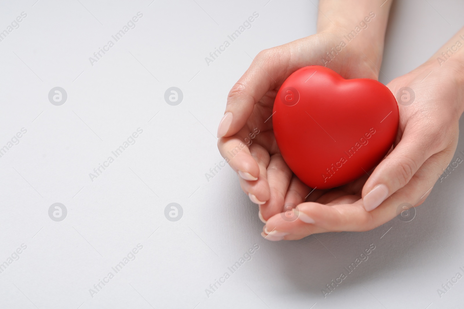 Photo of Woman holding red decorative heart on light grey background, closeup with space for text. Cardiology concept