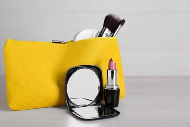 Photo of Stylish pocket mirror, lipstick and cosmetic bag with makeup products on white wooden table