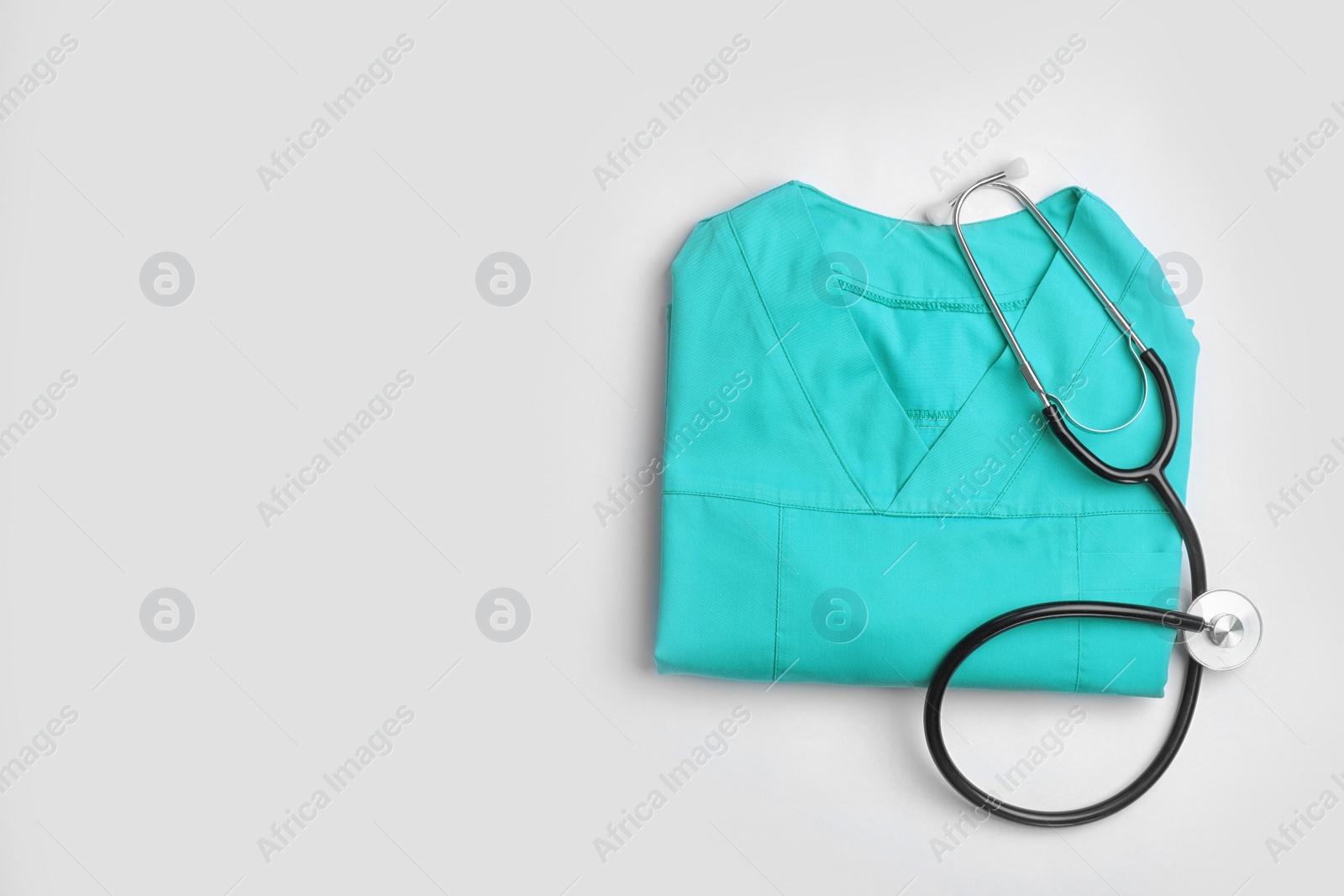 Photo of Folded medical uniform with stethoscope and space for text on white background, top view