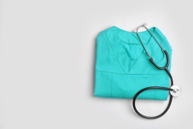 Photo of Folded medical uniform with stethoscope and space for text on white background, top view