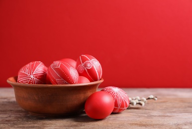Photo of Wooden bowl with red painted Easter eggs on table against color background, space for text
