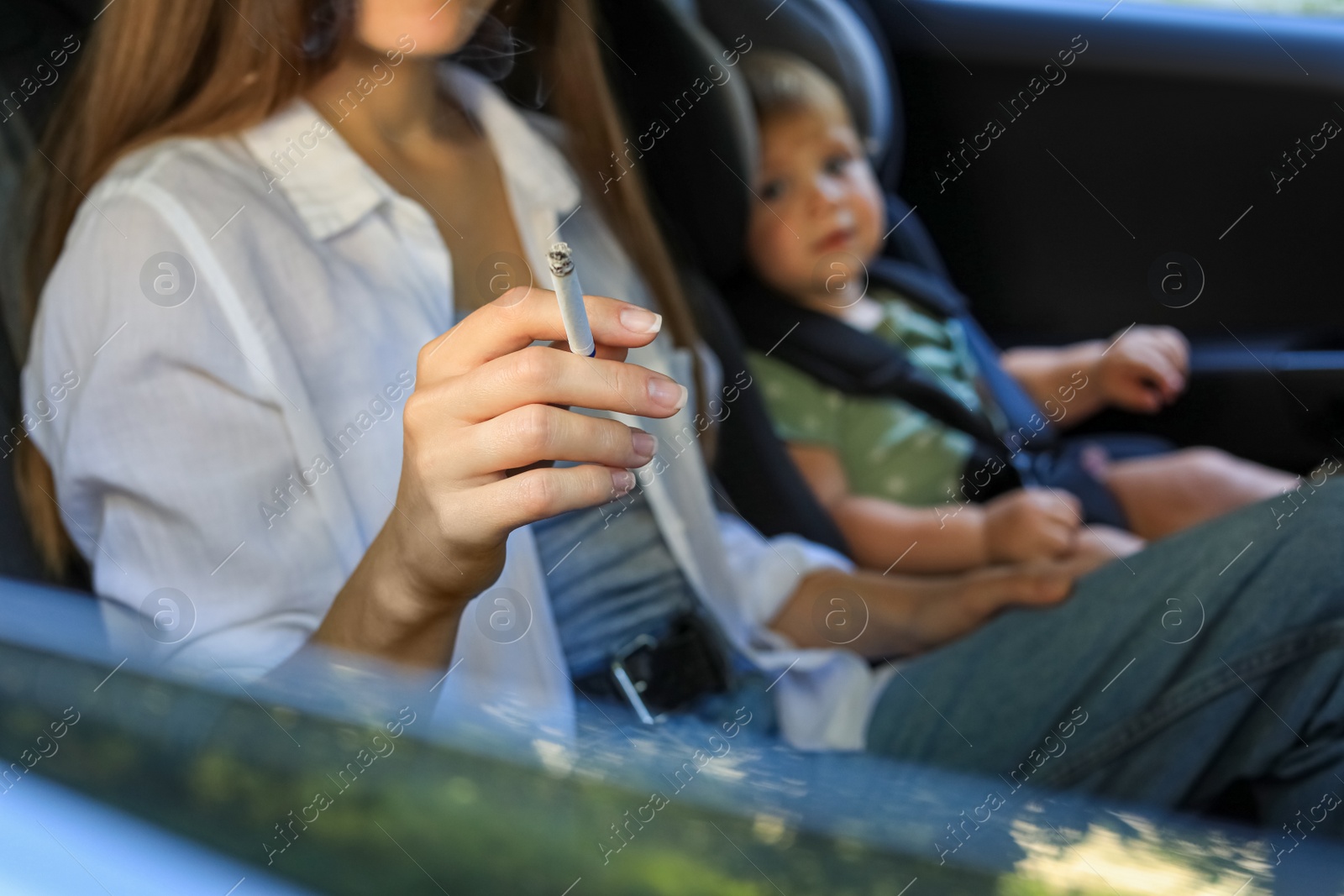 Photo of Mother with cigarette and child in car, closeup. Don't smoke near kids