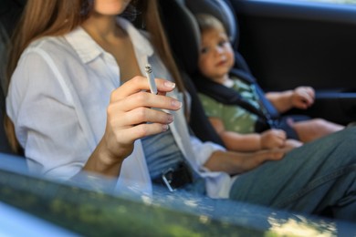 Photo of Mother with cigarette and child in car, closeup. Don't smoke near kids