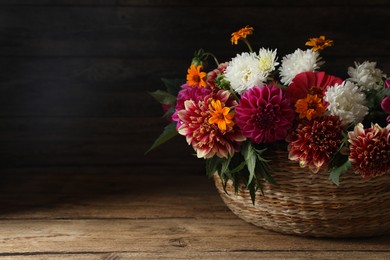 Photo of Beautiful wild flowers and leaves in wicker basket on wooden table. Space for text
