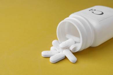 Photo of Overturned jar of calcium supplement pills on yellow background, closeup. Space for text