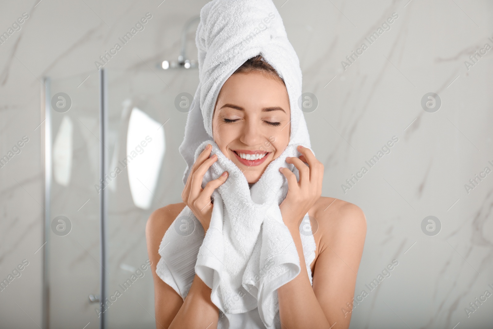 Photo of Young woman wiping face with towel in bathroom