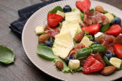 Tasty salad with brie cheese, prosciutto, almonds and berries on wooden table, closeup