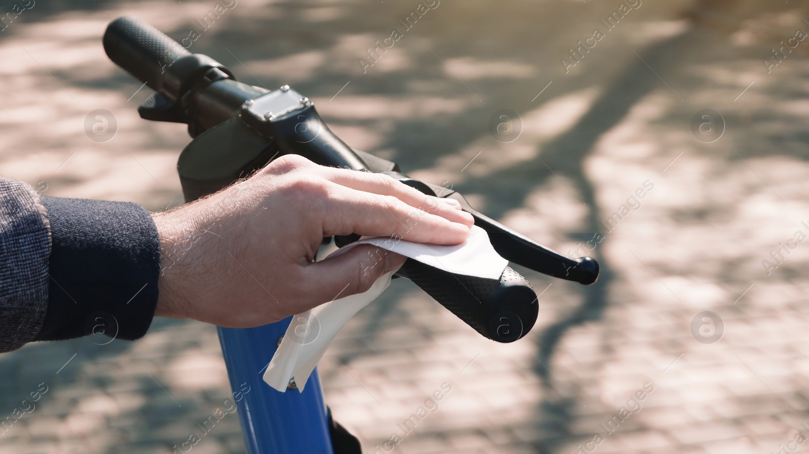 Photo of Man cleaning scooter steering wheel with wet wipe outdoors, closeup. Protective measures