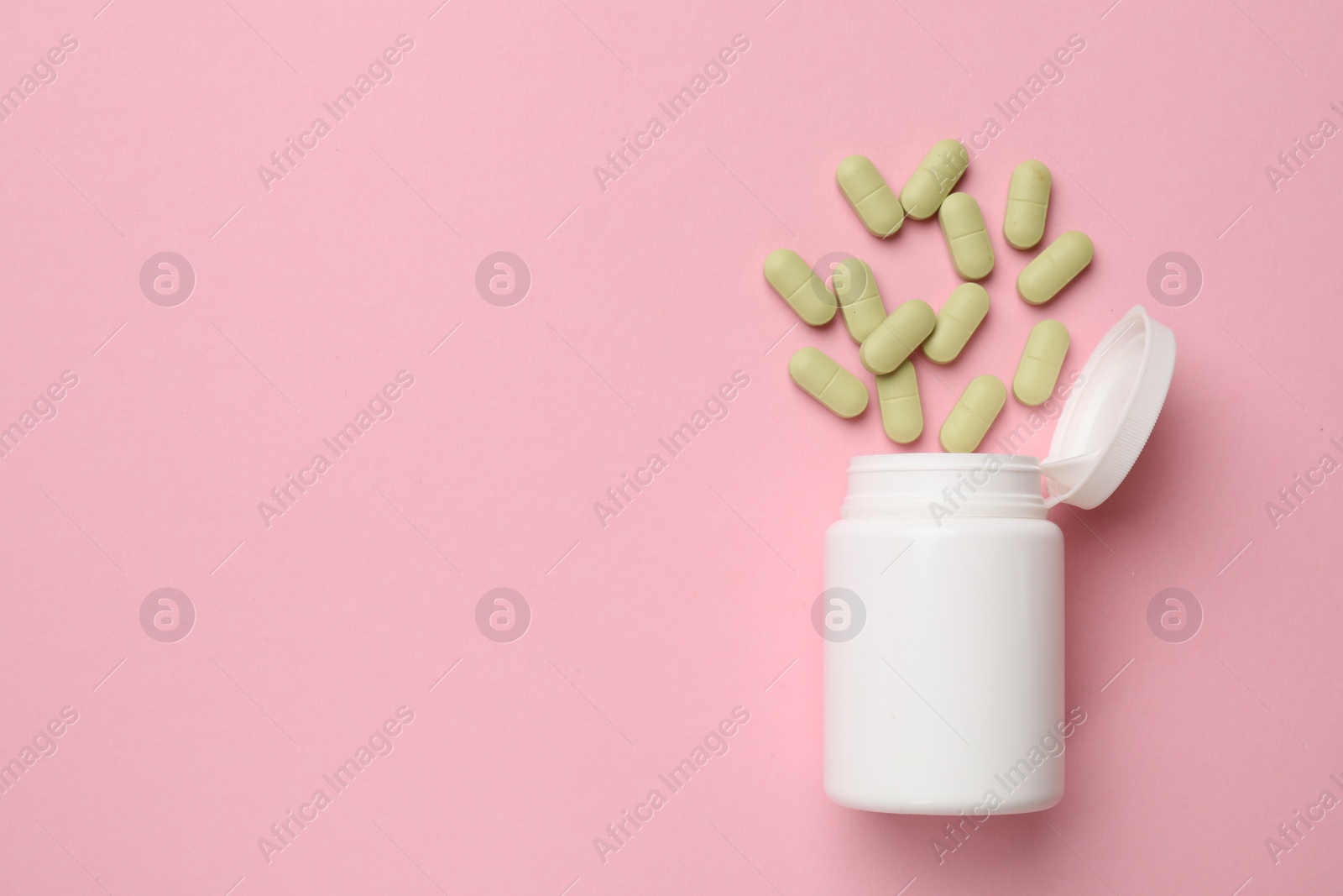 Photo of White bottle and different vitamin capsules on pink background, top view. Space for text