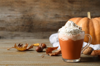 Photo of Pumpkin spice latte with whipped cream in glass cup on wooden table. Space for text