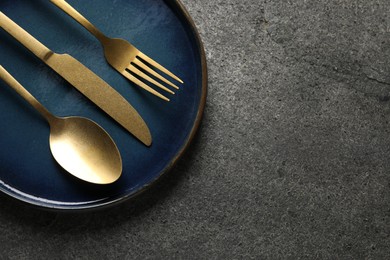 Photo of Stylish golden cutlery and plate on grey table, top view. Space for text