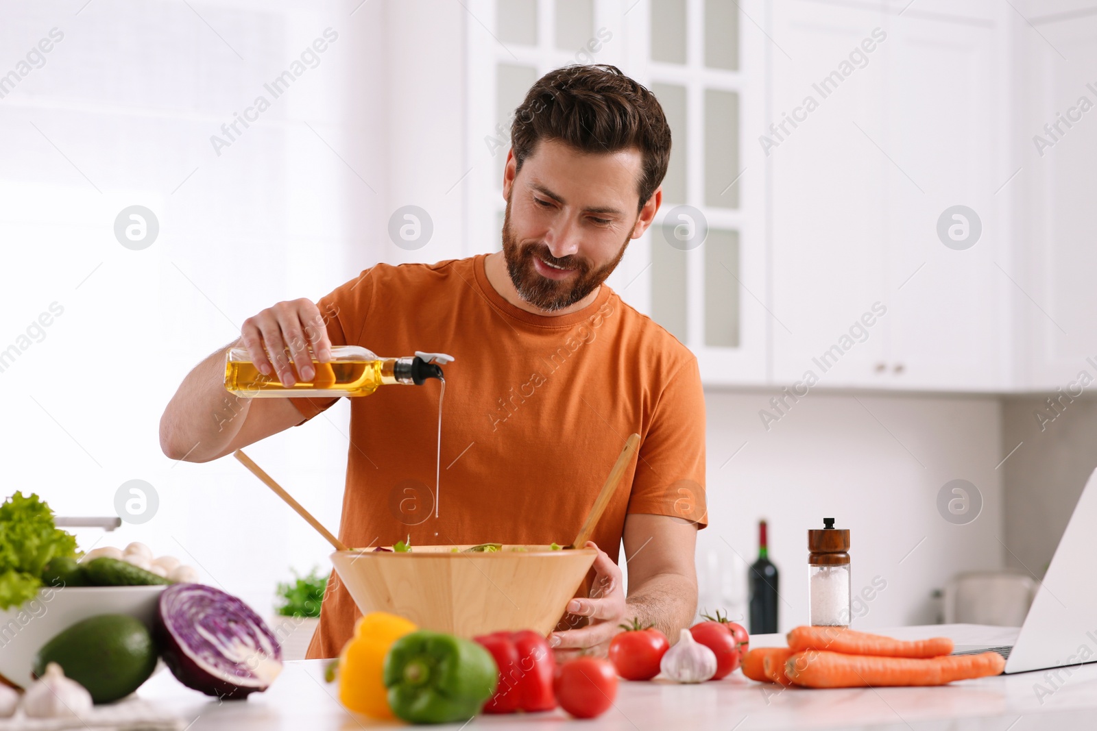 Photo of Man making dinner while watching online cooking course via laptop in kitchen