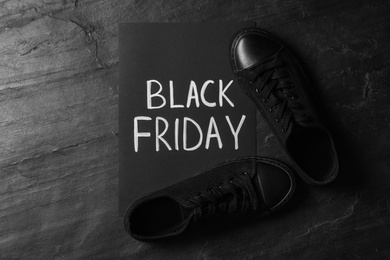 Photo of Sneakers and sheet of paper with words Black Friday on dark background, flat lay