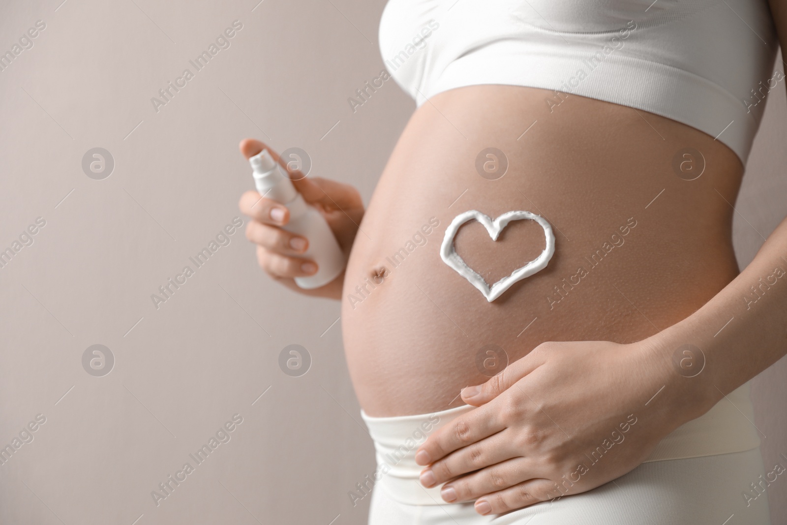 Photo of Young pregnant woman with cosmetic product on grey background, closeup. Space for text