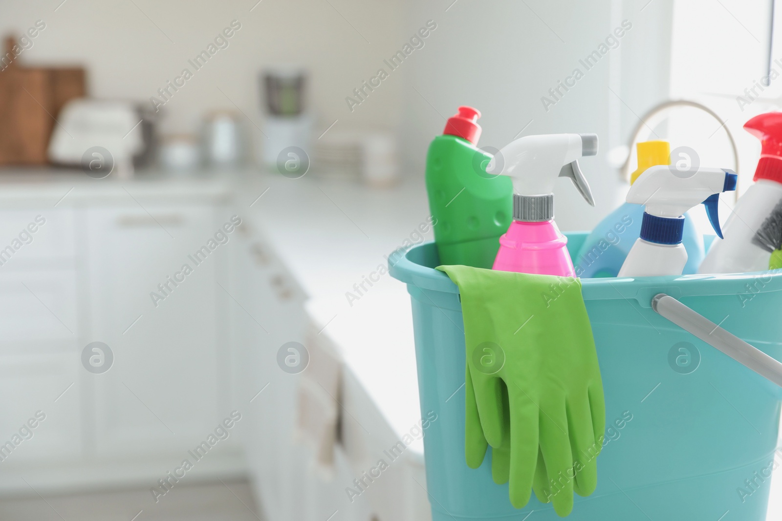 Photo of Plastic bucket with different cleaning supplies in kitchen, closeup. Space for text