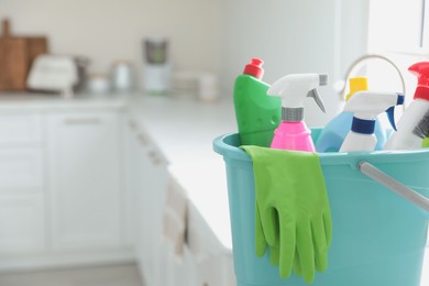 Photo of Plastic bucket with different cleaning supplies in kitchen, closeup. Space for text