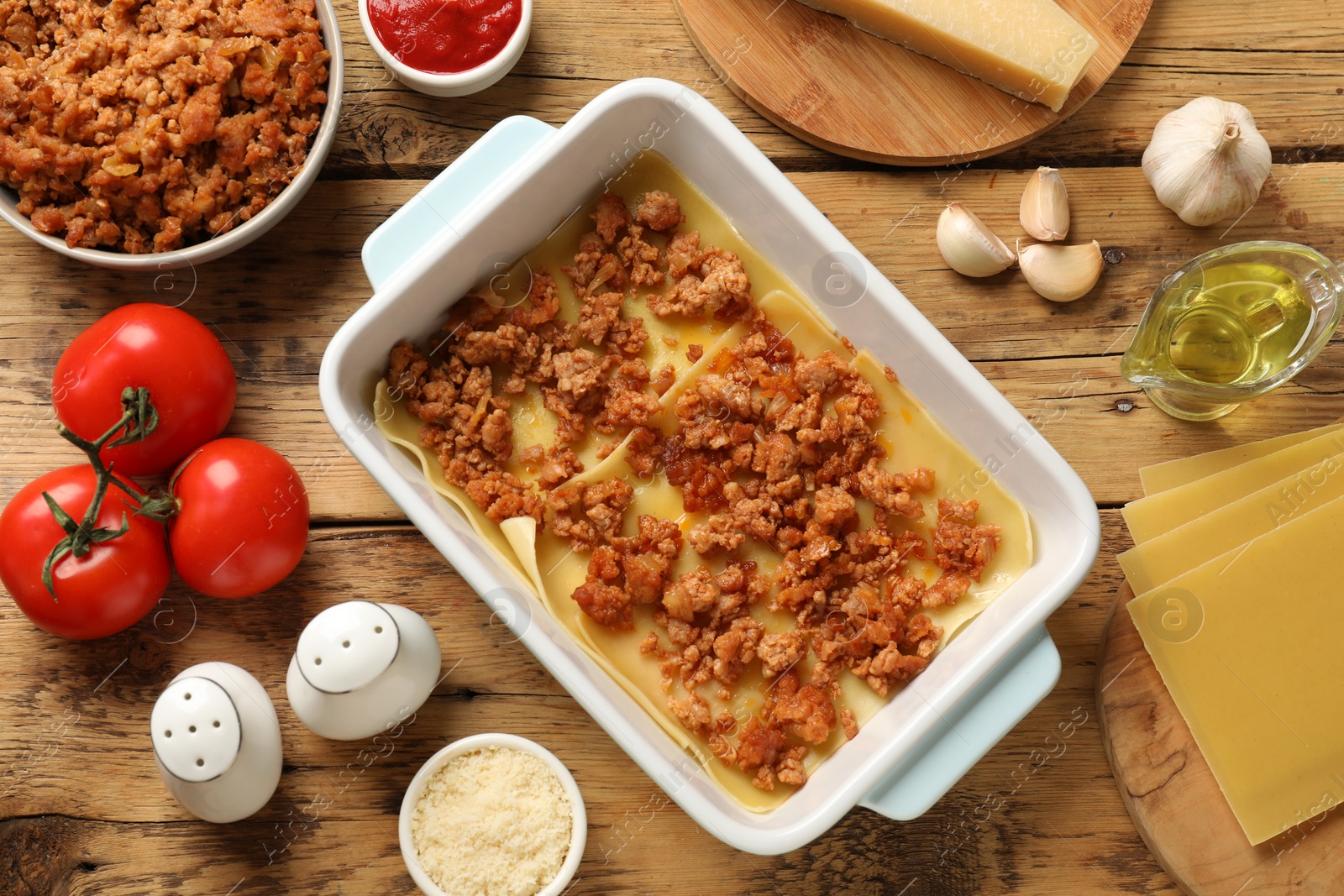 Photo of Cooking lasagna. Pasta sheets, minced meat in baking tray and products on wooden table, flat lay