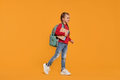 Happy schoolgirl with backpack and books on orange background