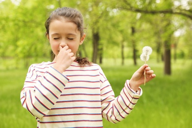 Little girl with dandelions suffering from seasonal allergy outdoors on sunny day