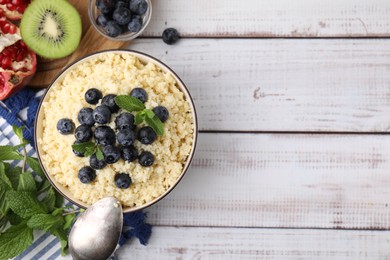 Photo of Bowl of tasty couscous with blueberries and mint served on white wooden table, flat lay. Space for text