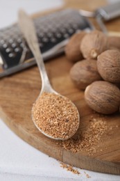 Spoon with grated nutmeg and seeds on white table, closeup
