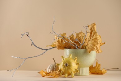 Composition with beautiful autumn leaves, tree branches and pumpkins on table against beige background