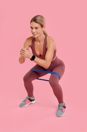 Photo of Woman exercising with elastic resistance band on pink background